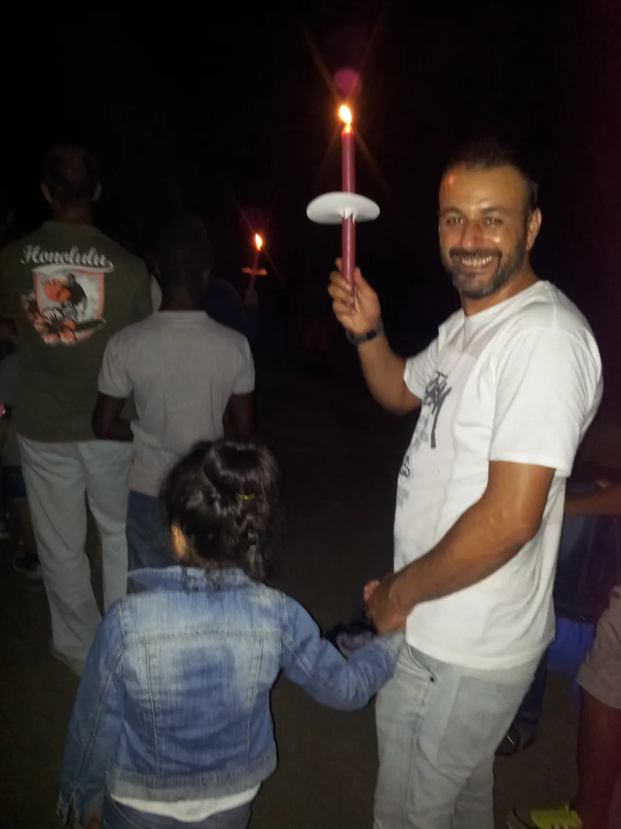 Alessandro sorride con una candela in mano, tenendo per mano la figlia durante una fiaccolata serale