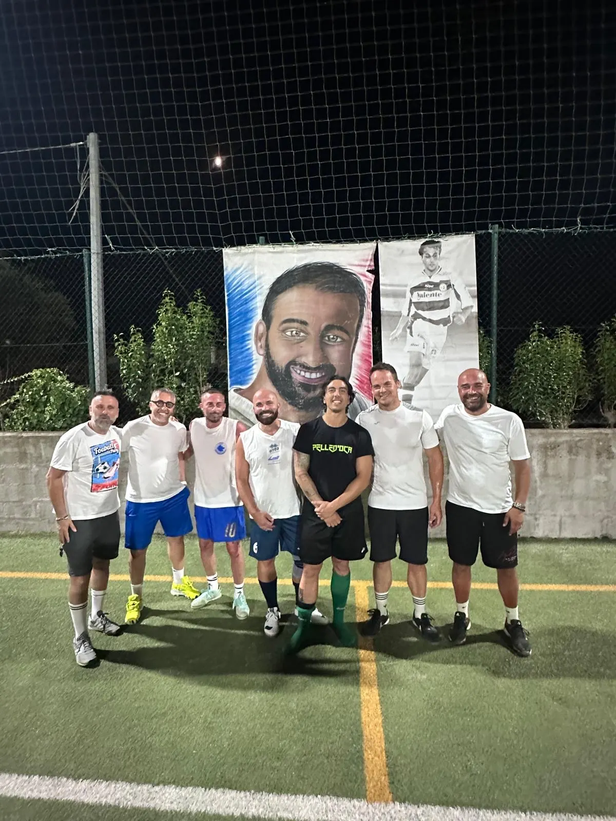 Sette partecipanti dell'edizione 2024 davanti al grande ritratto dipinto di Alessandro Morricella, in notturna