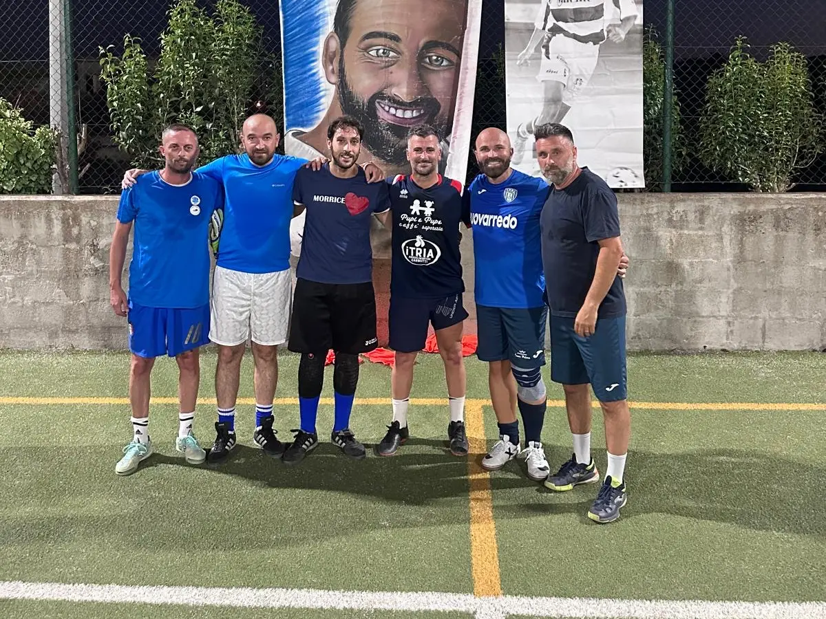 Giocatori dell'edizione 2024 del torneo, abbracciati sotto i teli dedicati ad Alessandro, in notturna